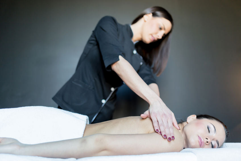 Young female massage therapist massaging a young lady laying on a massage table