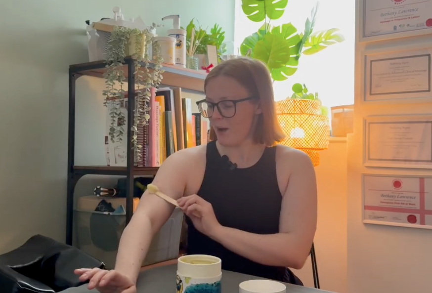 A practitioner demonstrating wax application on her arm using a disposable wooden spatula designed for Songbird products, supplied via Massage Warehouse across the UK and Ireland; illustrates hygienic single-treatment portion control using both ends of the utensil to eliminate cross-contamination risks during treatments in Brighton.