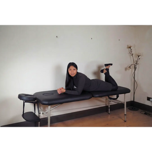 A professional therapist showcasing the durability of the black Advantage 10.5kg massage table in a home clinic setting in the UK.