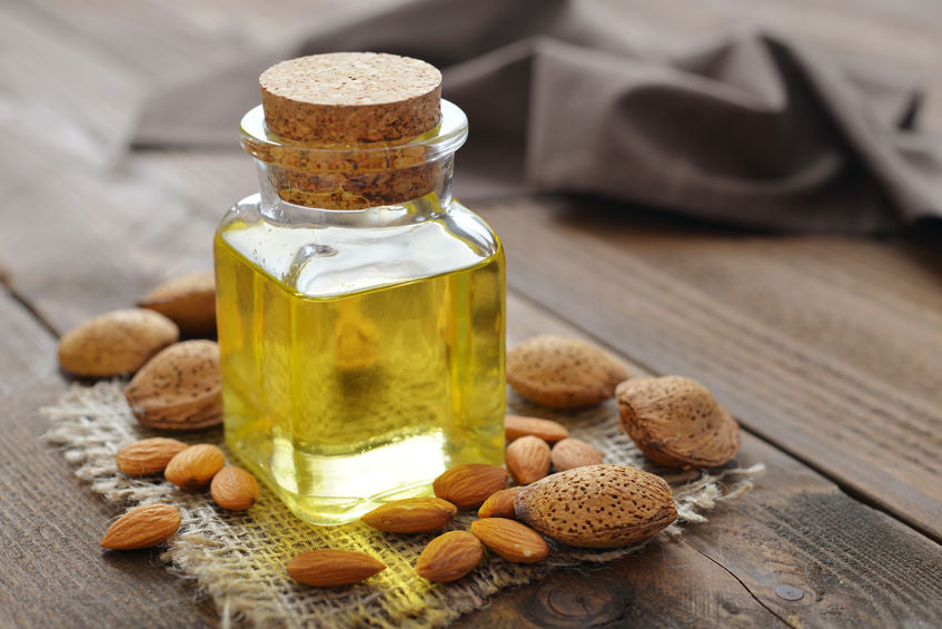 A bottle of oil stands on a wooden table surrounded by nuts of different sizes