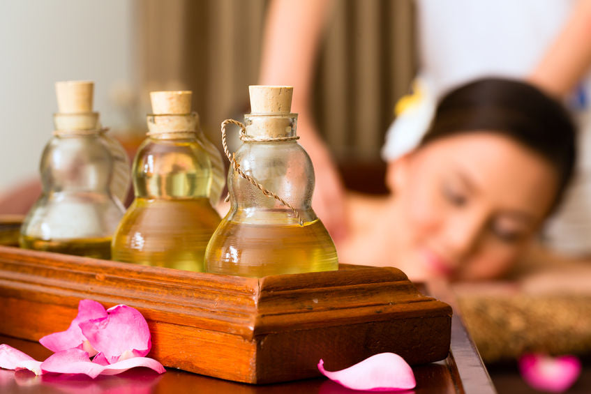 Three bottles of massage oil in a wooden box stand in front of a young woman enjoying a massage treatment