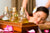 Three bottles of massage oil in a wooden box stand in front of a young woman enjoying a massage treatment