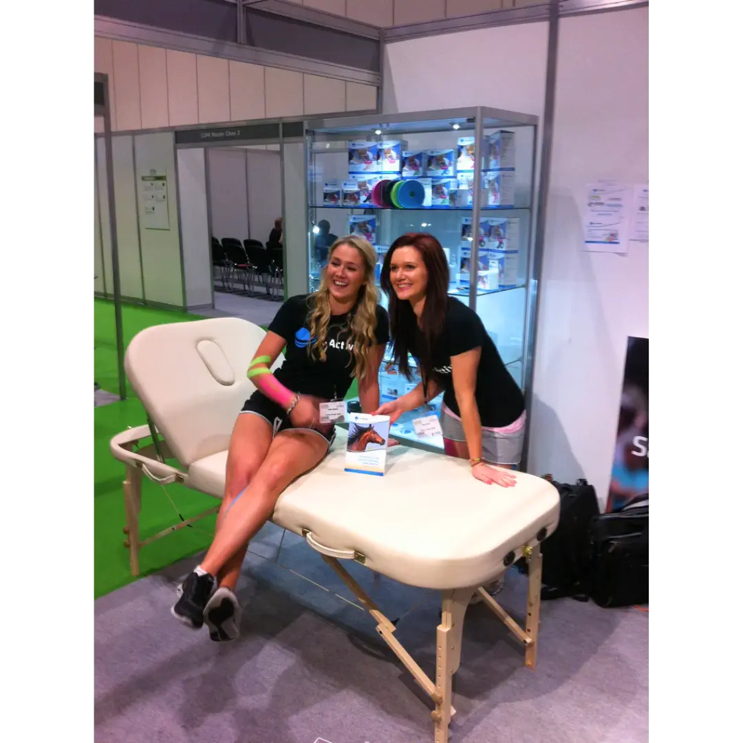 Cream-colored Earthworks Comfort Liftback portable massage table being demonstrated at a professional trade show in the United Kingdom.