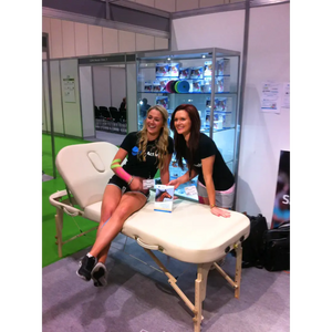 Cream-colored Earthworks Comfort Liftback portable massage table being demonstrated at a professional trade show in the United Kingdom.