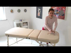 Therapist setting up a cream Earthworks Comfort Liftback massage table with an adjustable face cradle and matching bolster in the United Kingdom.