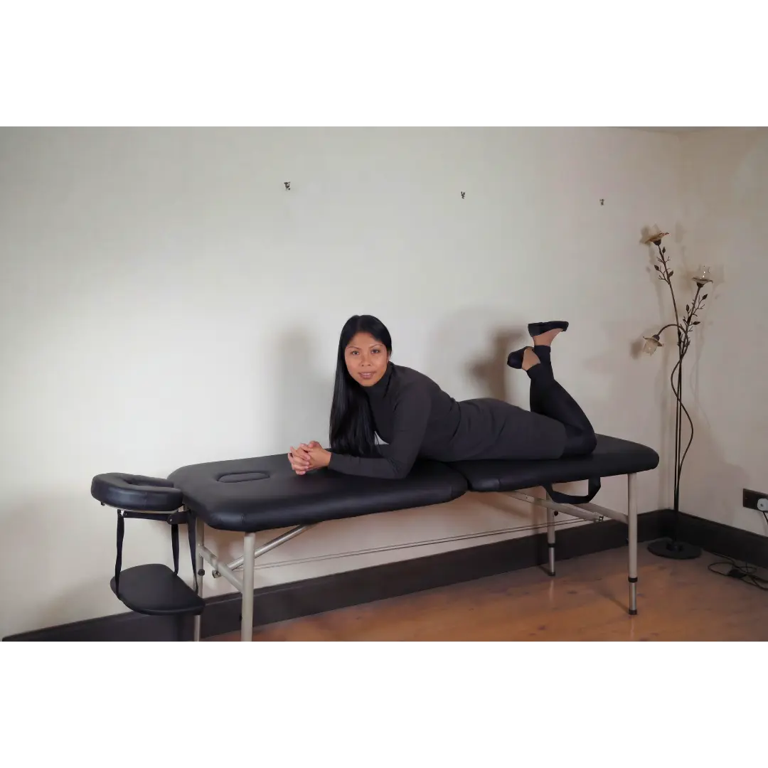 A professional therapist showcasing the durability of the black Advantage 10.5kg massage table in a home clinic setting in the UK.